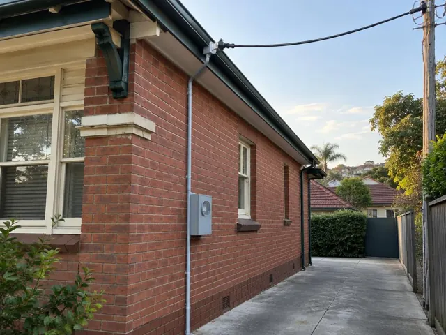 Brick house exterior with new overhead service cable and point-of-attachment bracket on the wall in Coogee